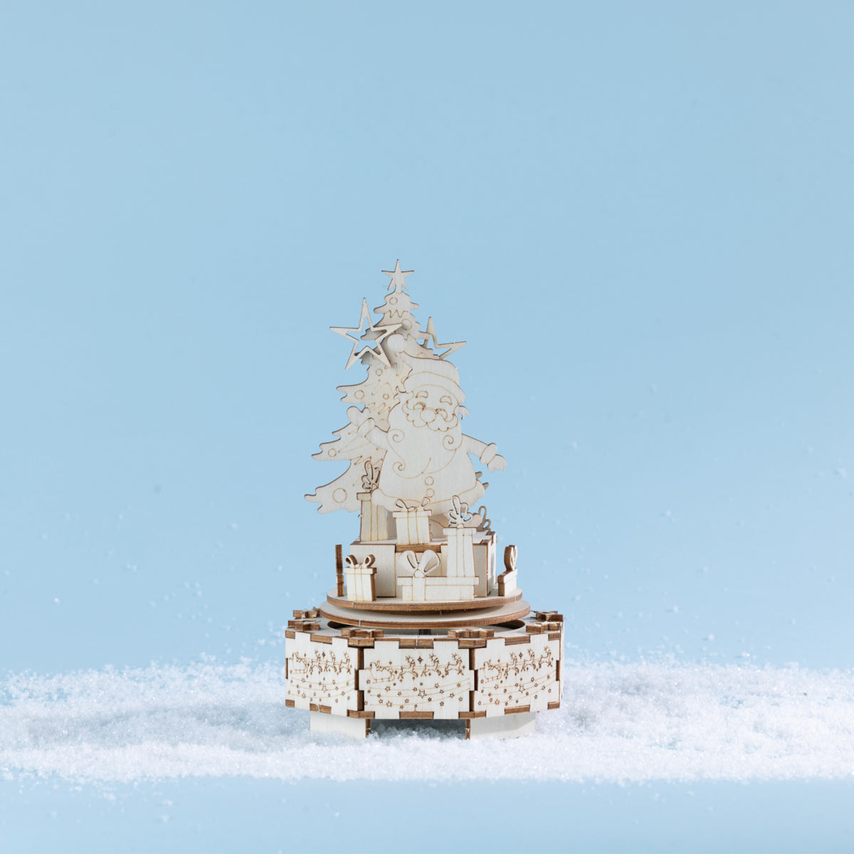 Completed wooden Santa music box featuring Santa beside a decorated Christmas tree and surrounded by stacked presents, all set on an intricately detailed festive base. Styled amongst faux snow against a soft blue backdrop.