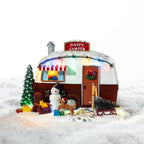 A whimsical illuminated Christmas camper scene featuring a snowman, reindeer, festive tree and colourful lights nestled in a snowy setting.