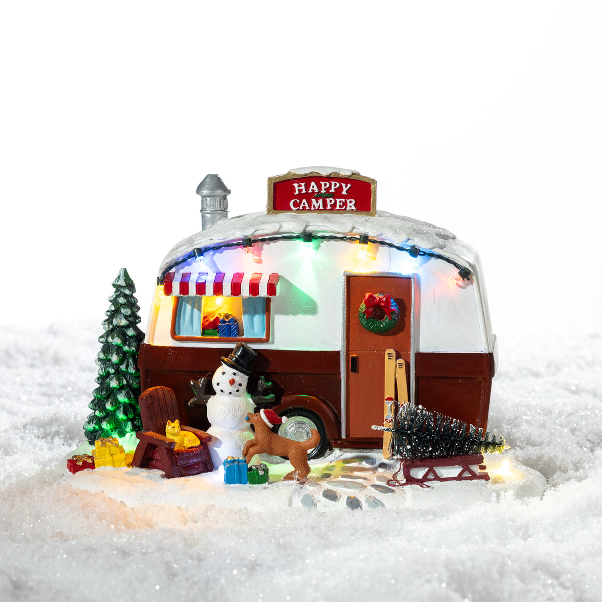 A whimsical illuminated Christmas camper scene featuring a snowman, reindeer, festive tree and colourful lights nestled in a snowy setting.