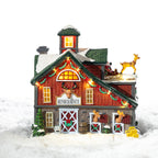 A whimsical illuminated Reindeer Rescue barn featuring festive garlands, cosy glowing windows and adorable reindeer nestled in a snowy setting.