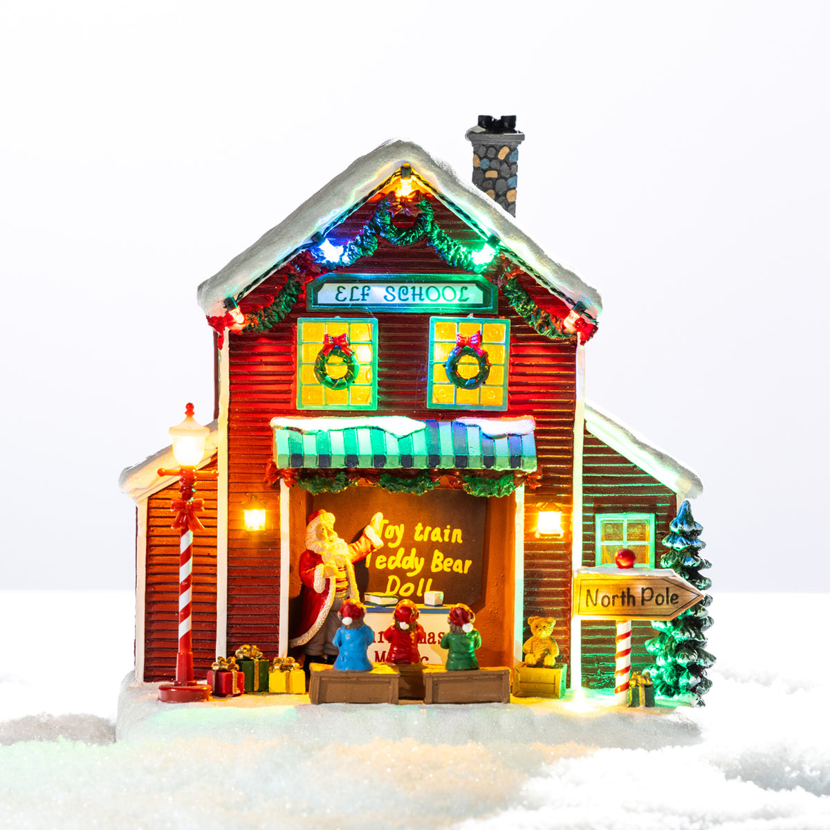 A whimsical illuminated Elf School featuring colourful Christmas lights, tiny elves, festive gifts and playful North Pole details in a snowy setting.