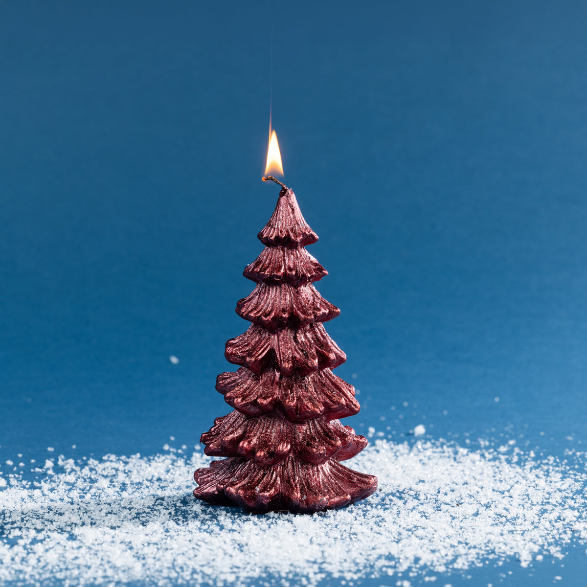 Decorative Christmas tree-shaped candle in a deep metallic red finish, featuring layered textured branches and a lit wick.