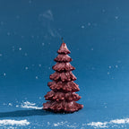 Deep red Christmas tree-shaped candle shown after extinguishing, with delicate smoke rising from the wick against a festive blue backdrop.