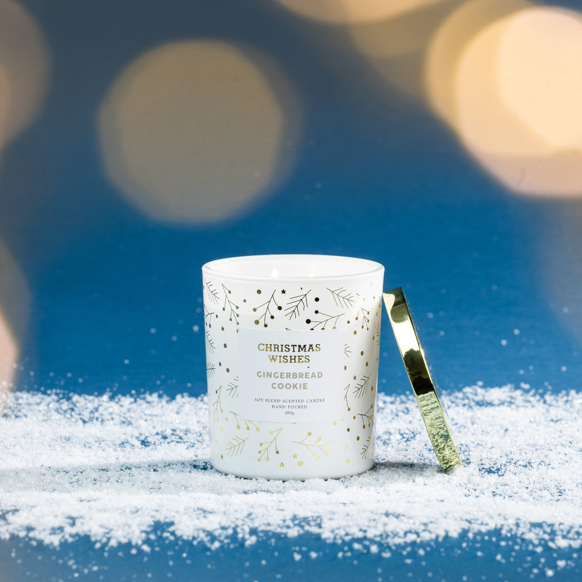 Christmas Wishes Gingerbread Cookie 283g scented candle in white glass, lit and displayed on faux snow against a blue background with warm festive lights.