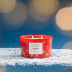 Christmas Wishes Cinnamon Apple 453g scented candle lit with multiple wicks against a festive blue background with warm blurred lights.