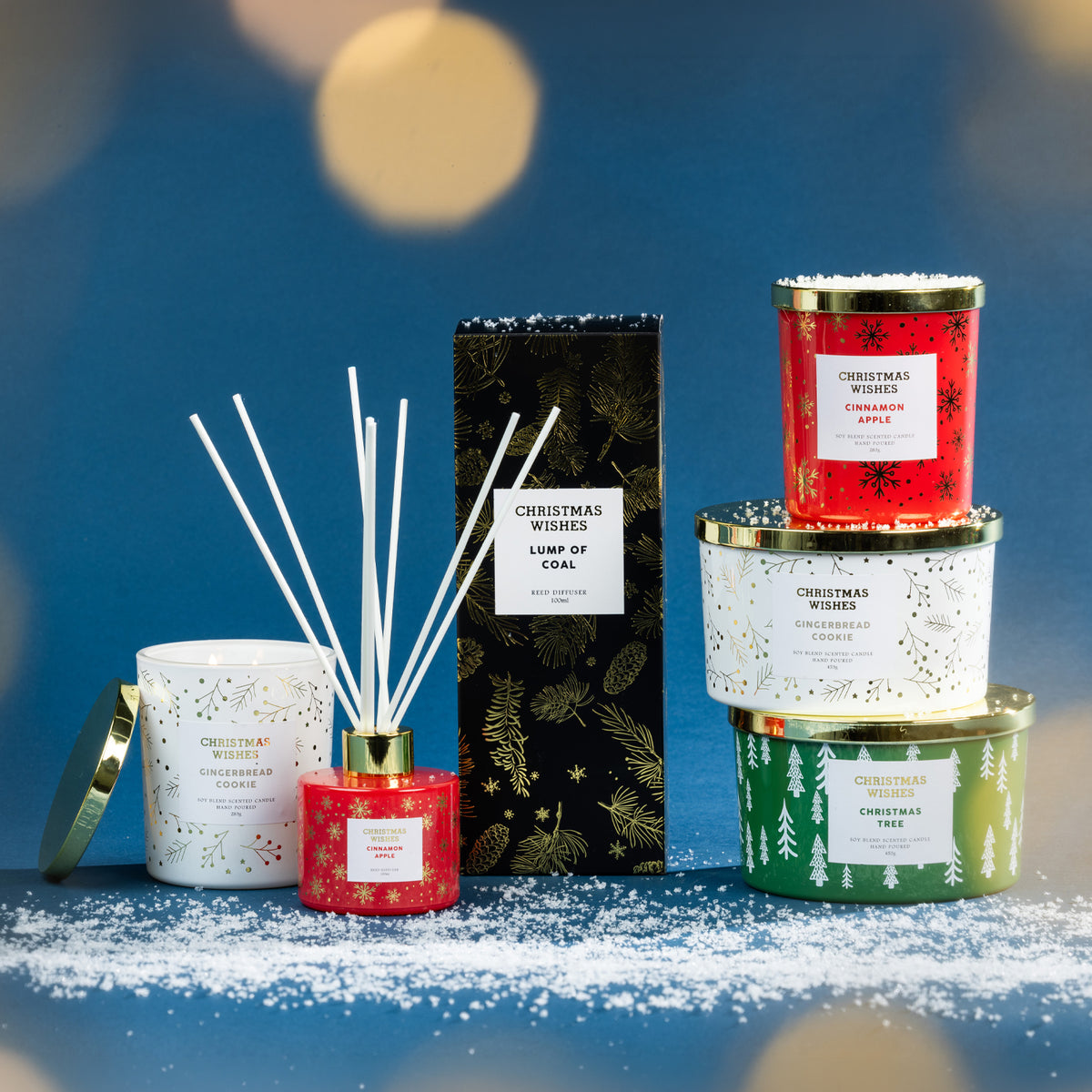 Christmas Wishes festive fragrance collection featuring coordinating candles and reed diffusers displayed together on a snowy blue backdrop.