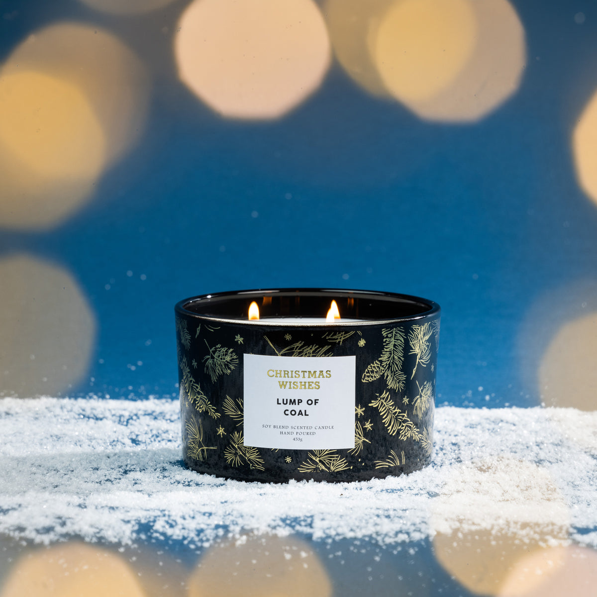 Christmas Wishes Lump of Coal 453g scented candle lit with multiple wicks against a festive blue background with warm blurred lights.