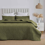 Olive green quilted coverlet set styled on a bed in a neutral bedroom.