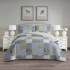 Patchwork coverlet set in blue, green and grey tones styled on a bed with matching pillowcases in a neutral bedroom.