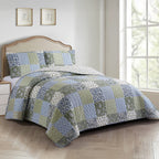 Patchwork coverlet set in blue, green and grey tones styled on a bed with matching pillowcases in a neutral bedroom.