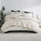 Natural coverlet set styled on a bed with matching pillows with a striped white duvet cover underneath in a neutral bedroom.