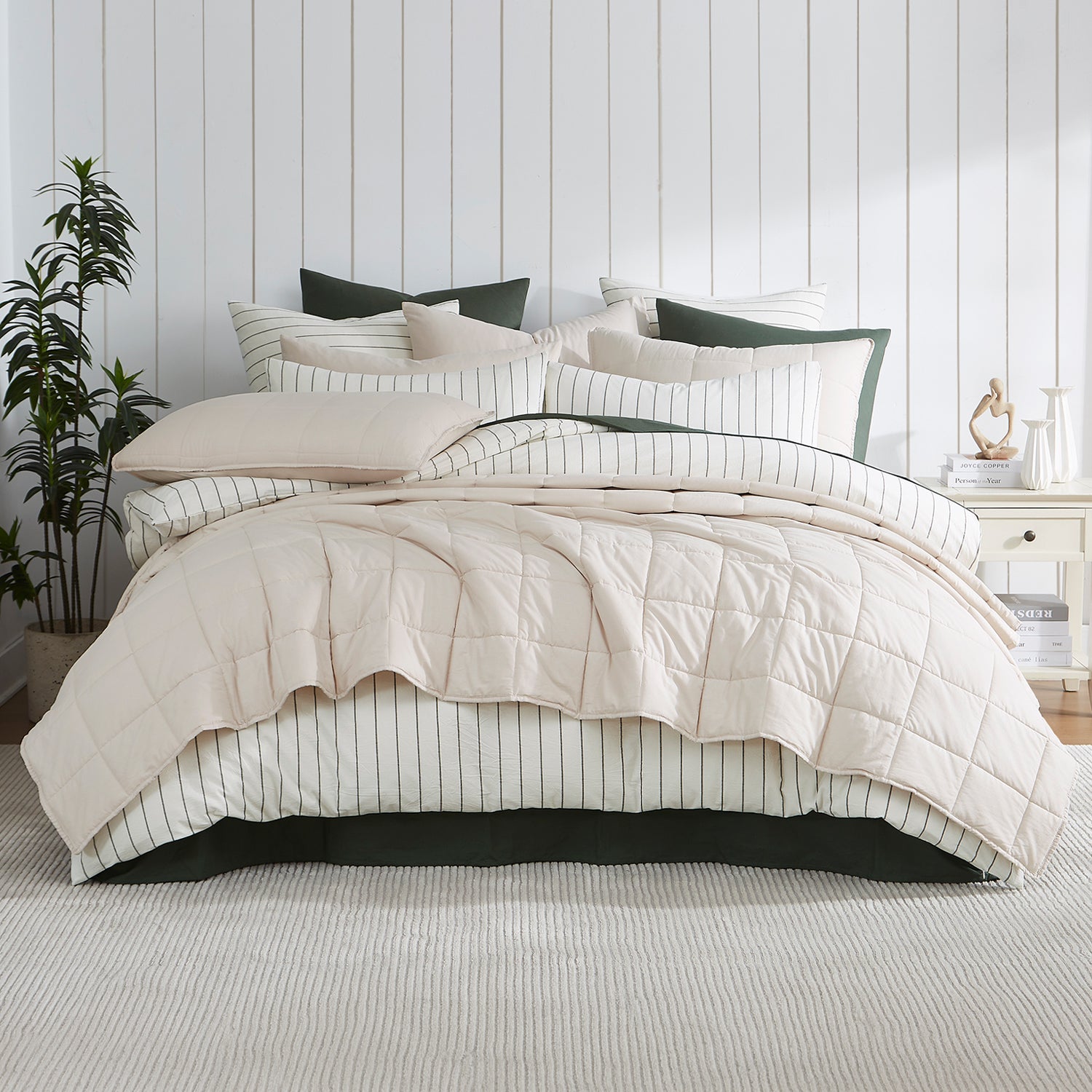 Natural coverlet set styled on a bed with matching pillows with a striped white duvet cover underneath in a neutral bedroom.