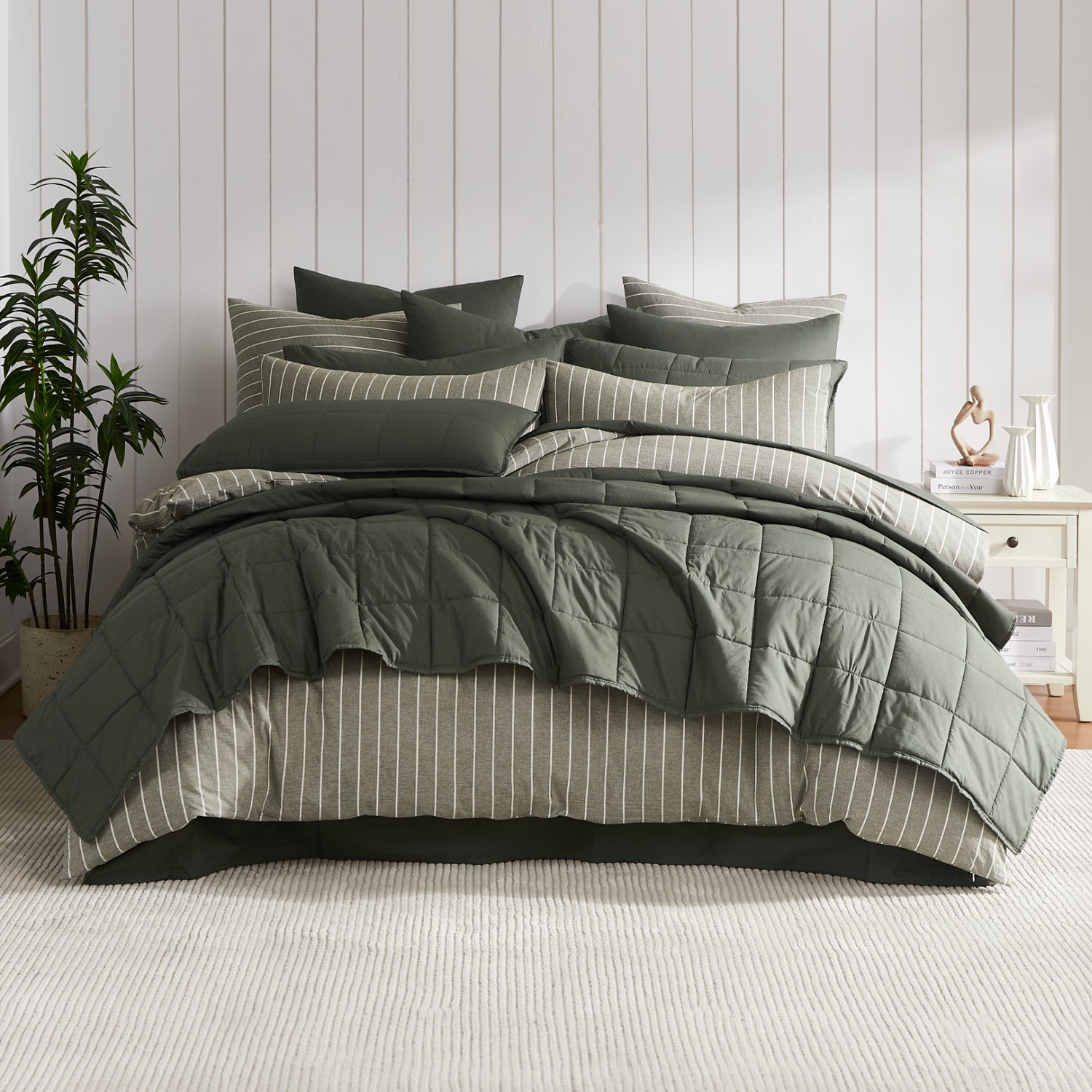 Thyme coverlet set styled on a bed with matching pillows with a striped green duvet cover underneath in a neutral bedroom.