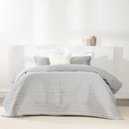 Bed styled with a soft silver quilted coverlet set featuring horizontal stitched detailing and matching pillow shams.