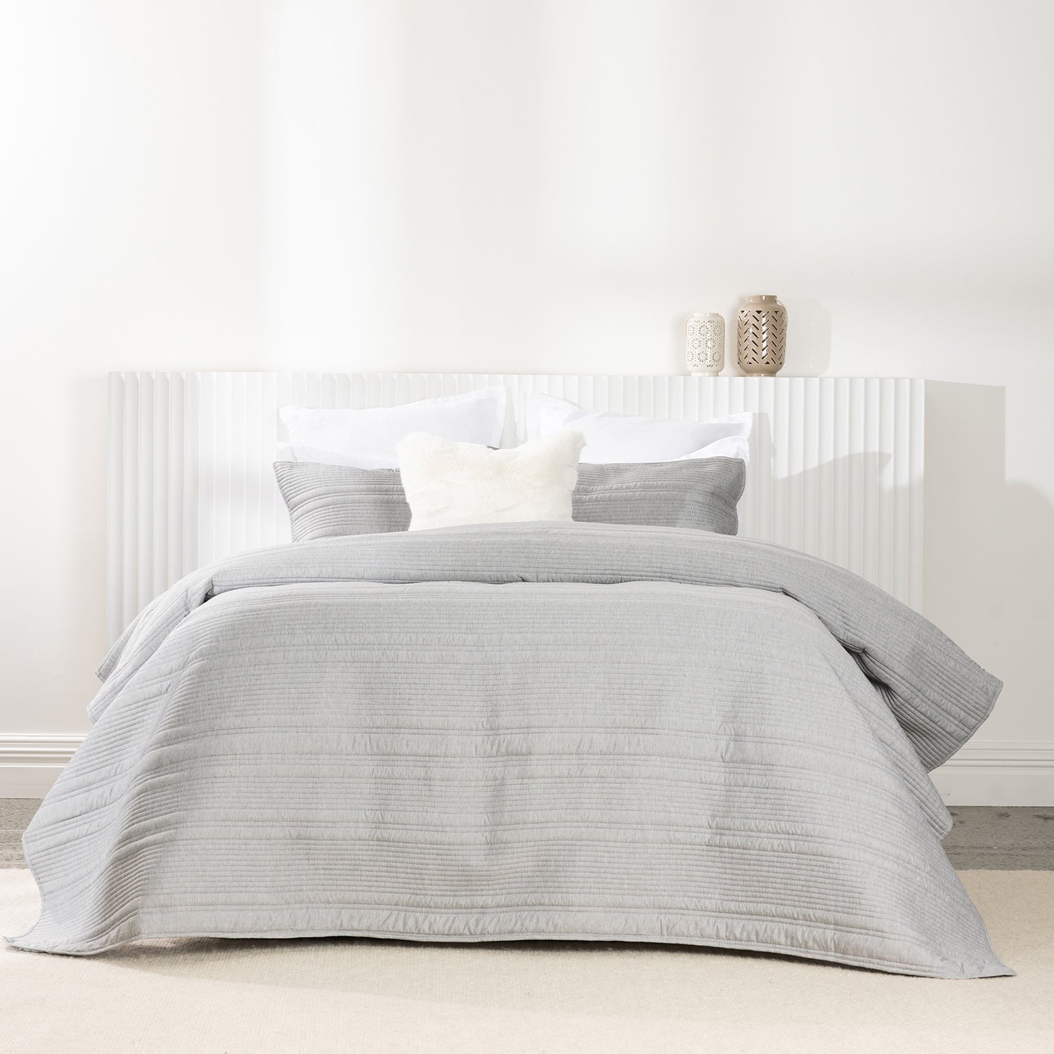 Bed styled with a soft silver quilted coverlet set featuring horizontal stitched detailing and matching pillow shams.