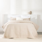 Bed styled with a soft natural quilted coverlet set featuring horizontal stitched detailing and matching pillow shams.