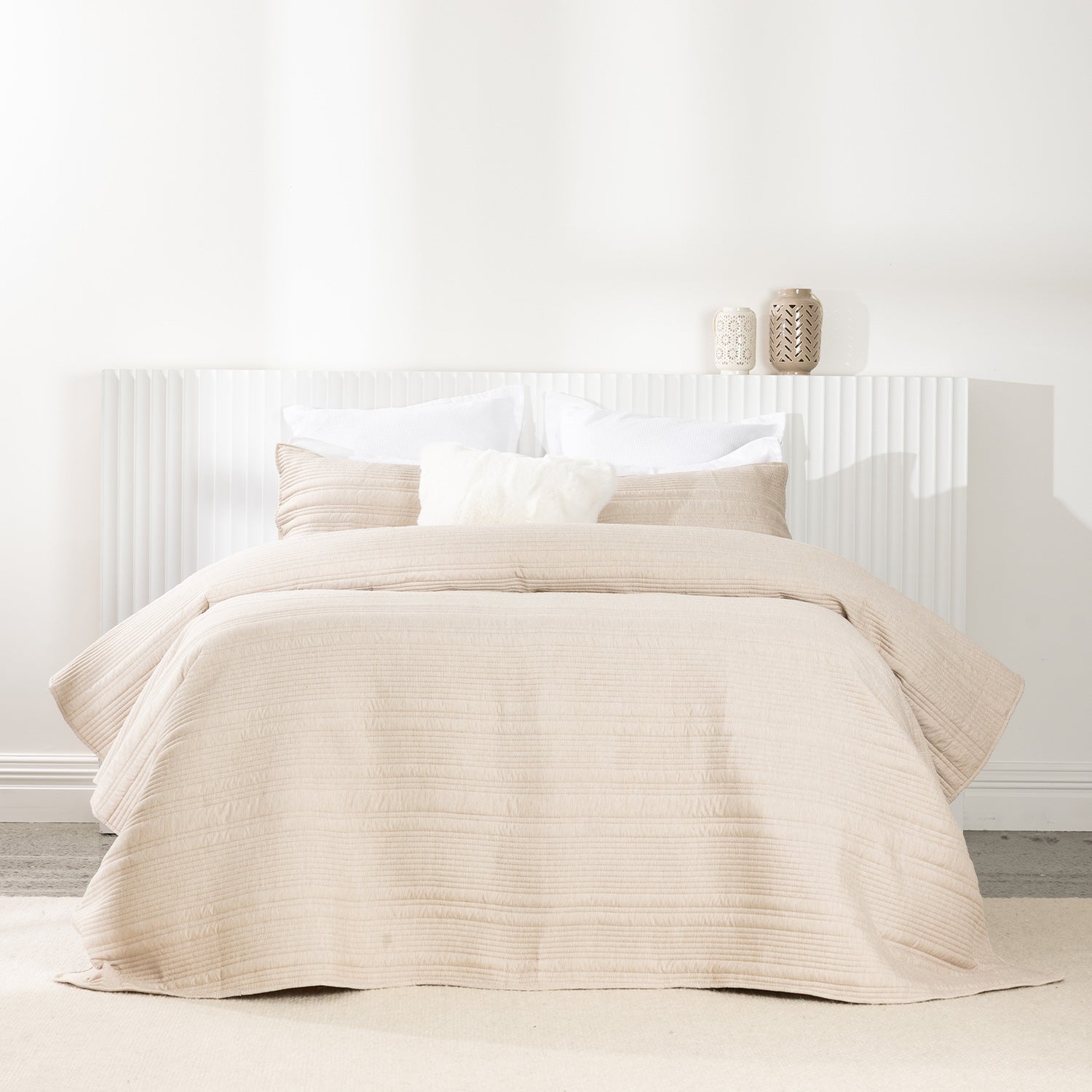 Bed styled with a soft natural quilted coverlet set featuring horizontal stitched detailing and matching pillow shams.