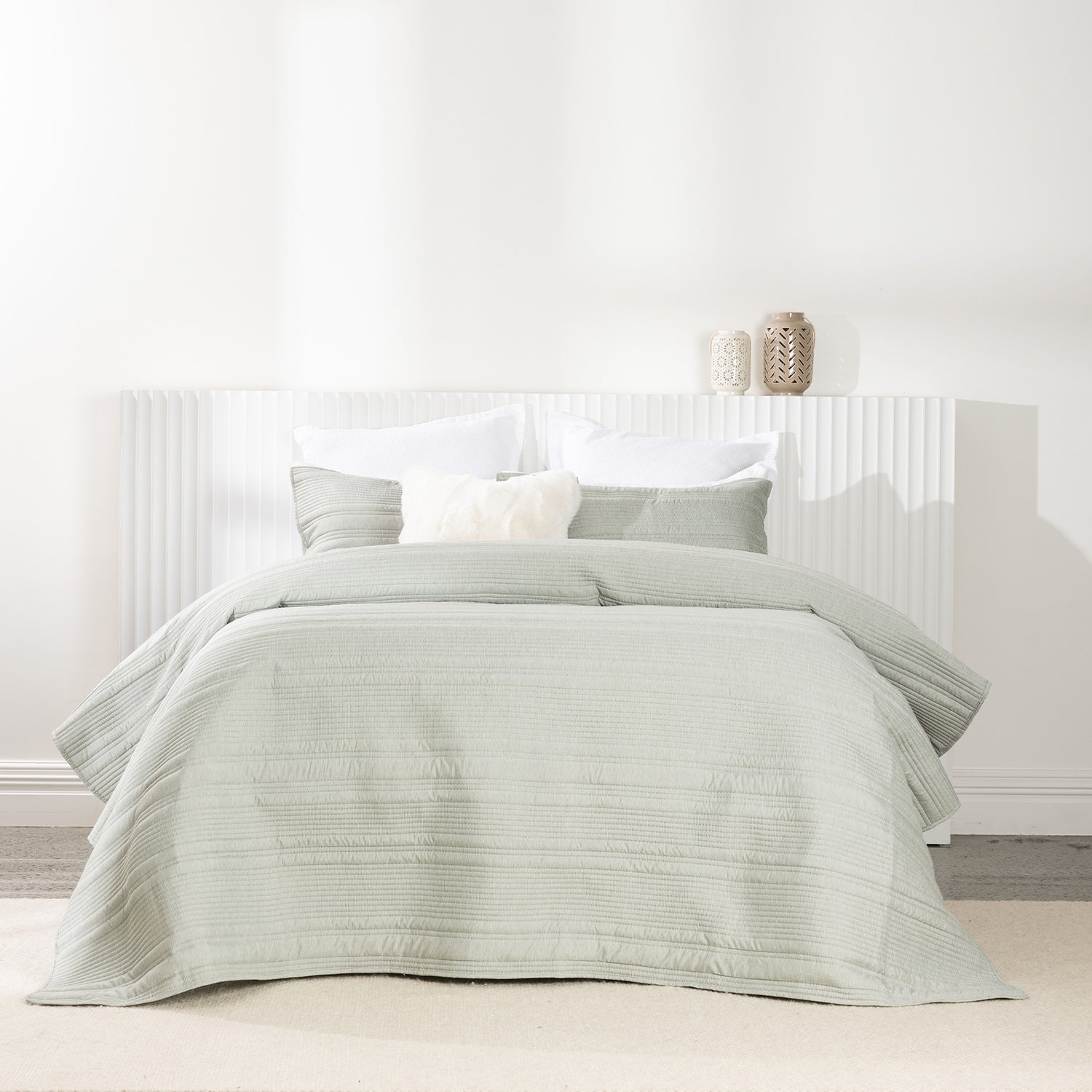 Bed styled with a soft sage quilted coverlet set featuring horizontal stitched detailing and matching pillow shams.