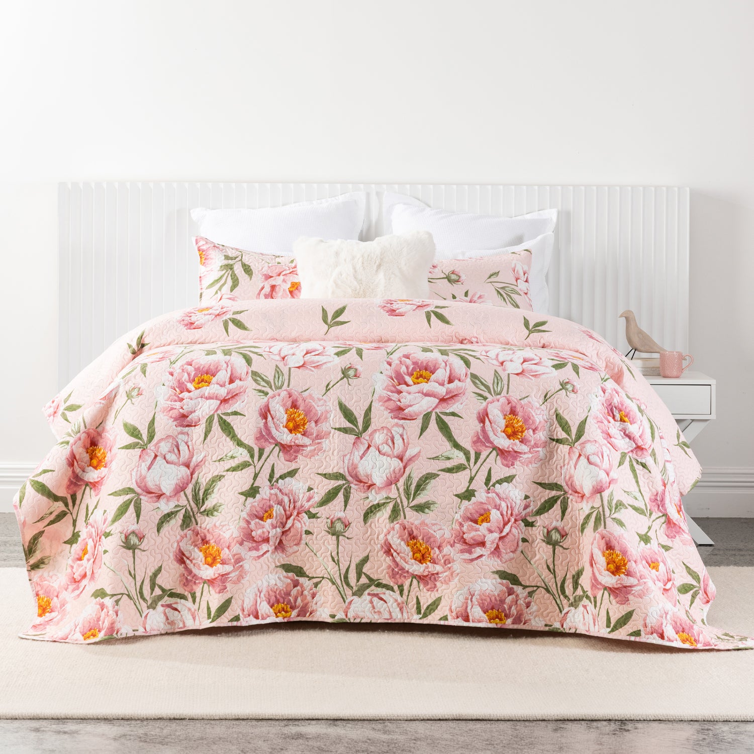 A soft blush pink coverlet set featuring oversized blooming peonies in shades of pink with green foliage creates a fresh, romantic look in a bright, contemporary bedroom.