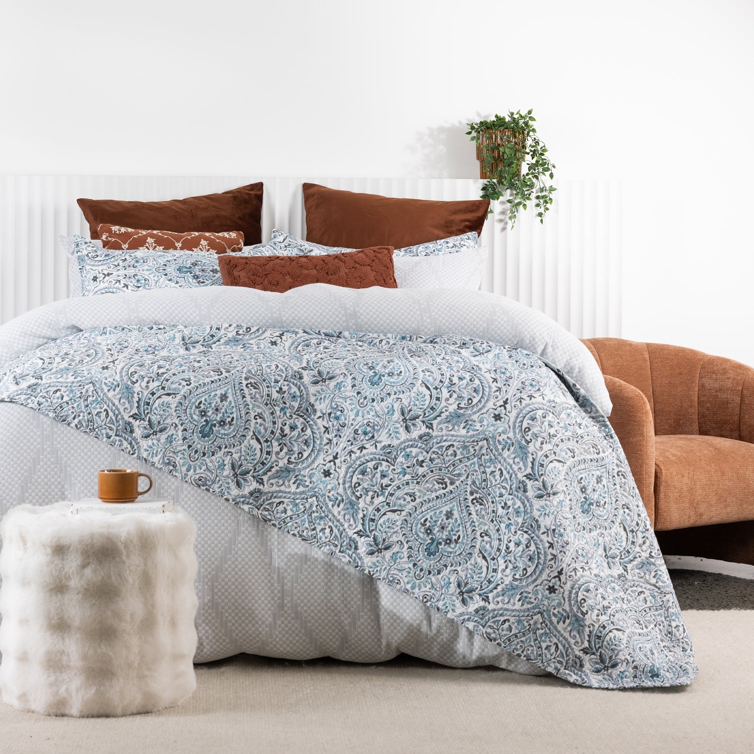 A blue and white paisley coverlet set layered over textured white bedding creates a fresh, elegant bedroom with warm earthy accents and timeless style.