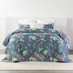 A vibrant floral coverlet set in rich denim blue with pink, cream and yellow blooms creates a bold, inviting bedroom with timeless botanical charm.