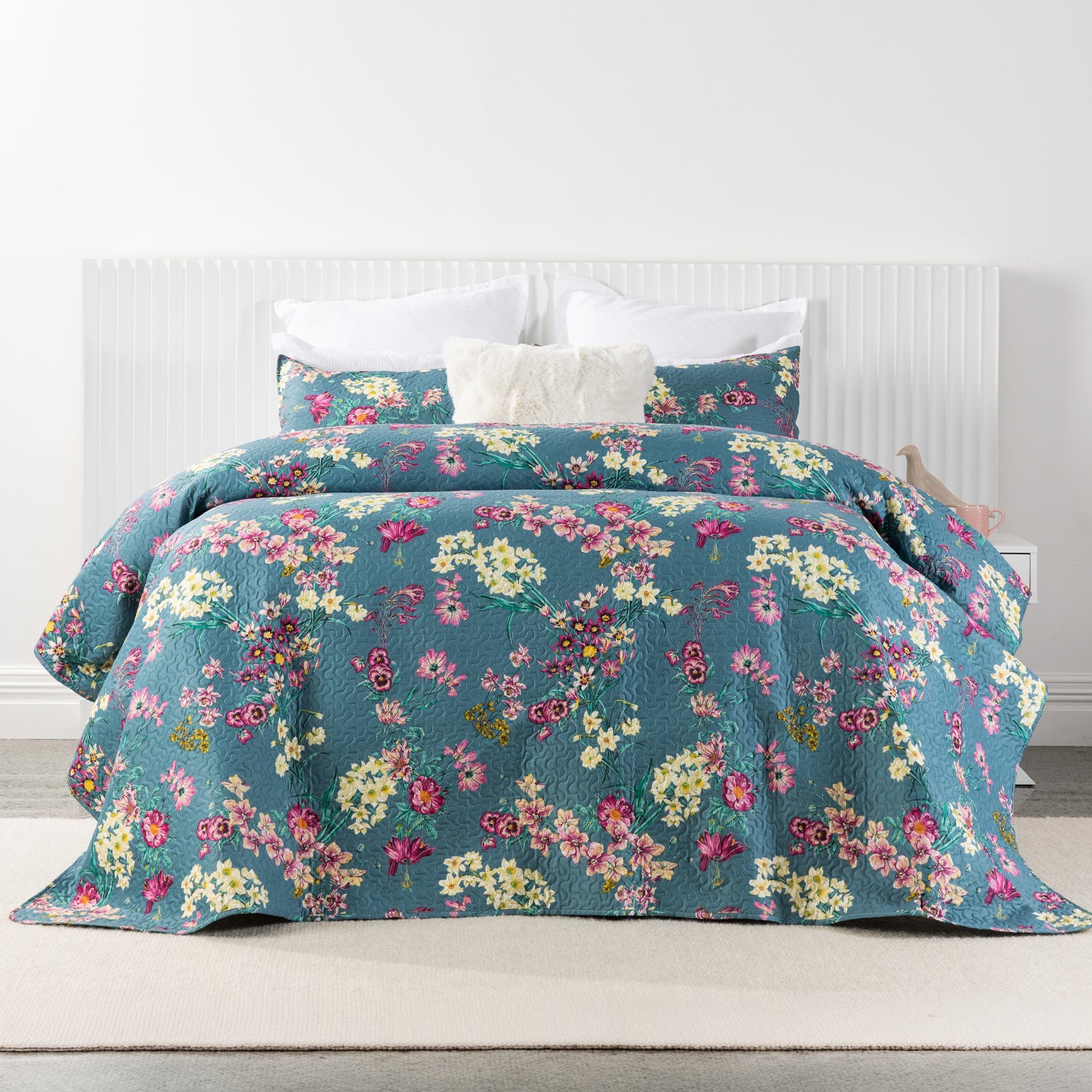 A vibrant floral coverlet set in rich denim blue with pink, cream and yellow blooms creates a bold, inviting bedroom with timeless botanical charm.