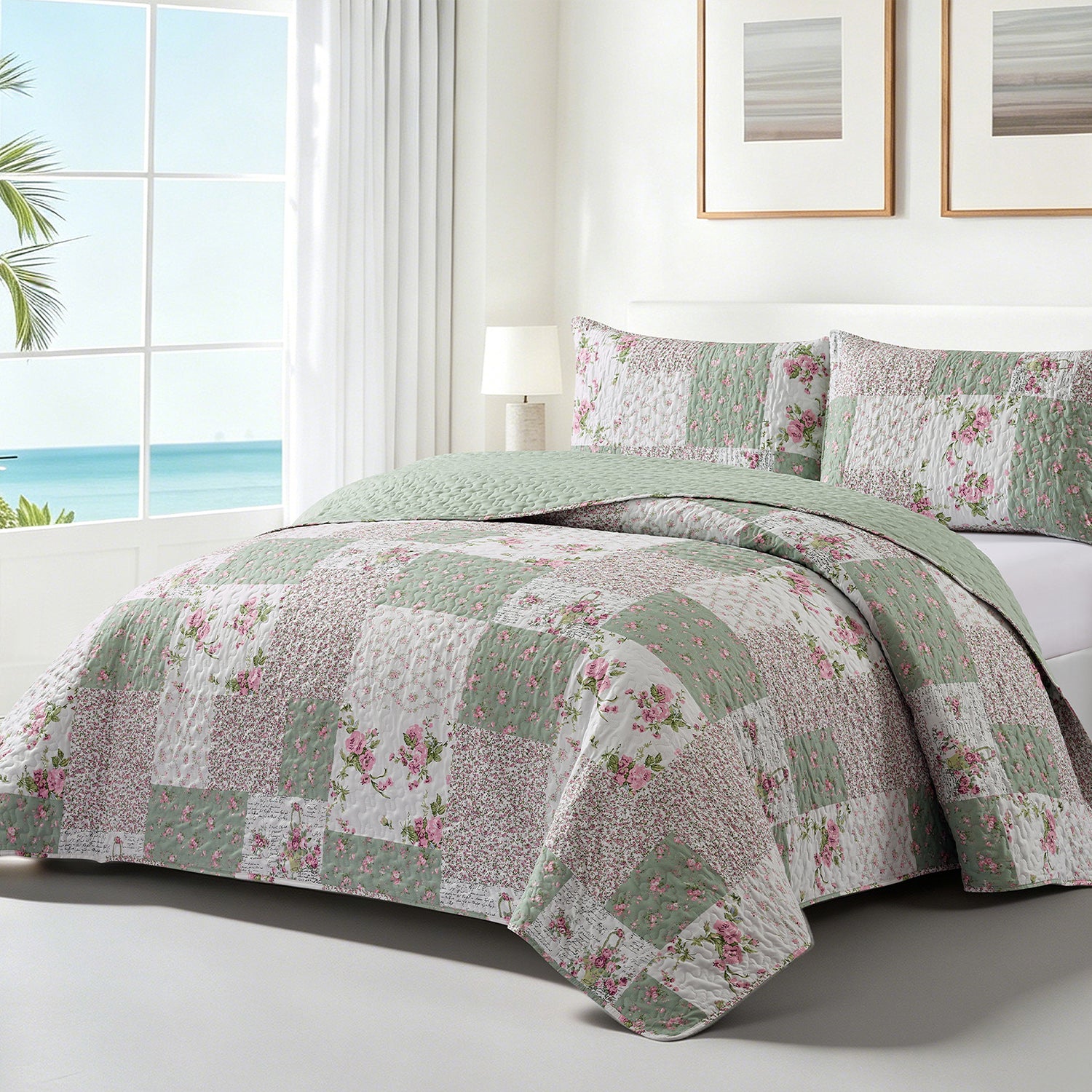 A patchwork quilted bedding set with a floral print in sage green, pink, and white, styled on a bed in a bright bedroom with a window overlooking the ocean.