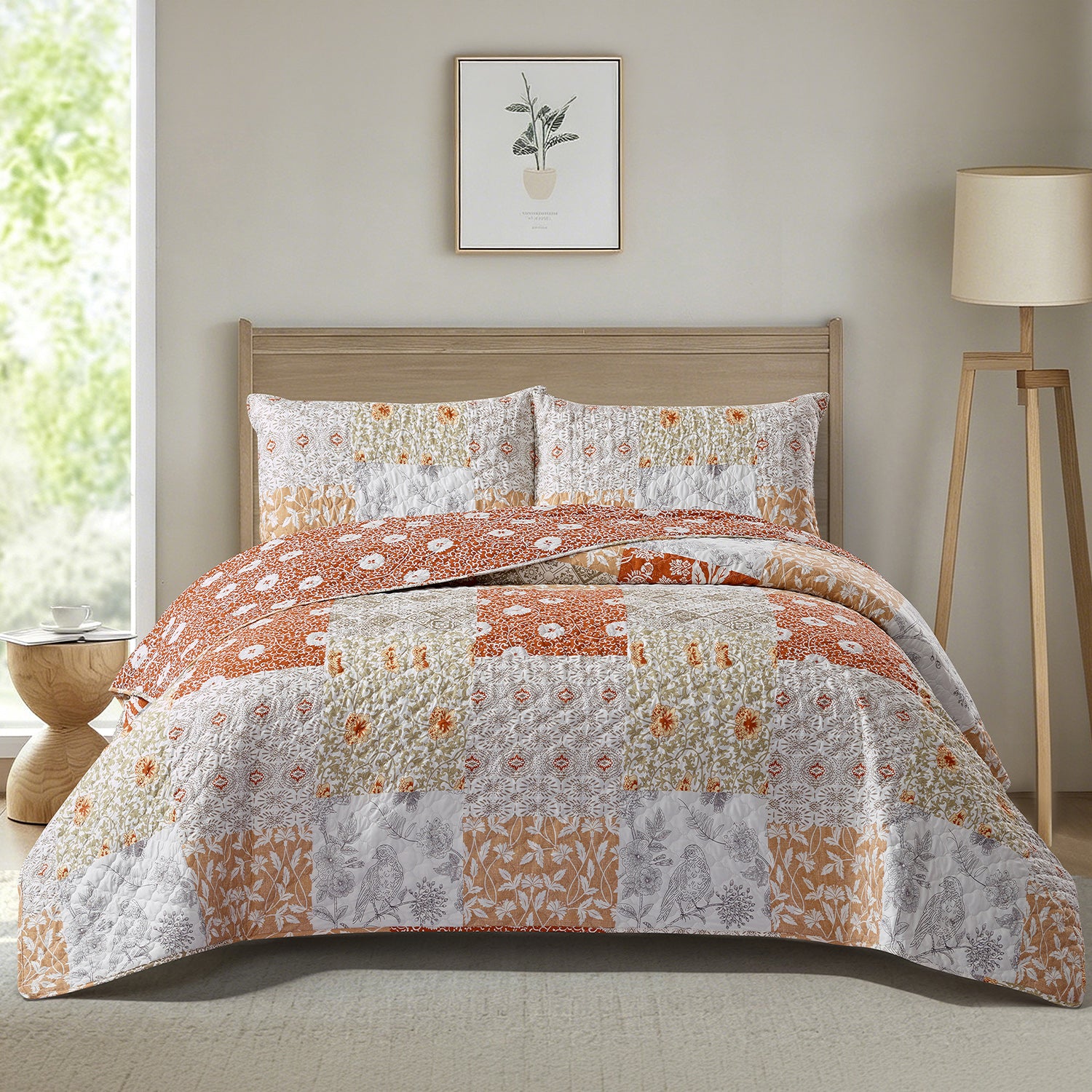 A patchwork quilted bedding set with a matching comforter and two shams, styled on a bed in a modern bedroom setting with a wooden floor lamp, side table, and framed botanical print on the wall.