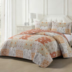 A patchwork quilt set in orange, beige, and white with matching shams, styled on a bed in a bright, modern bedroom.