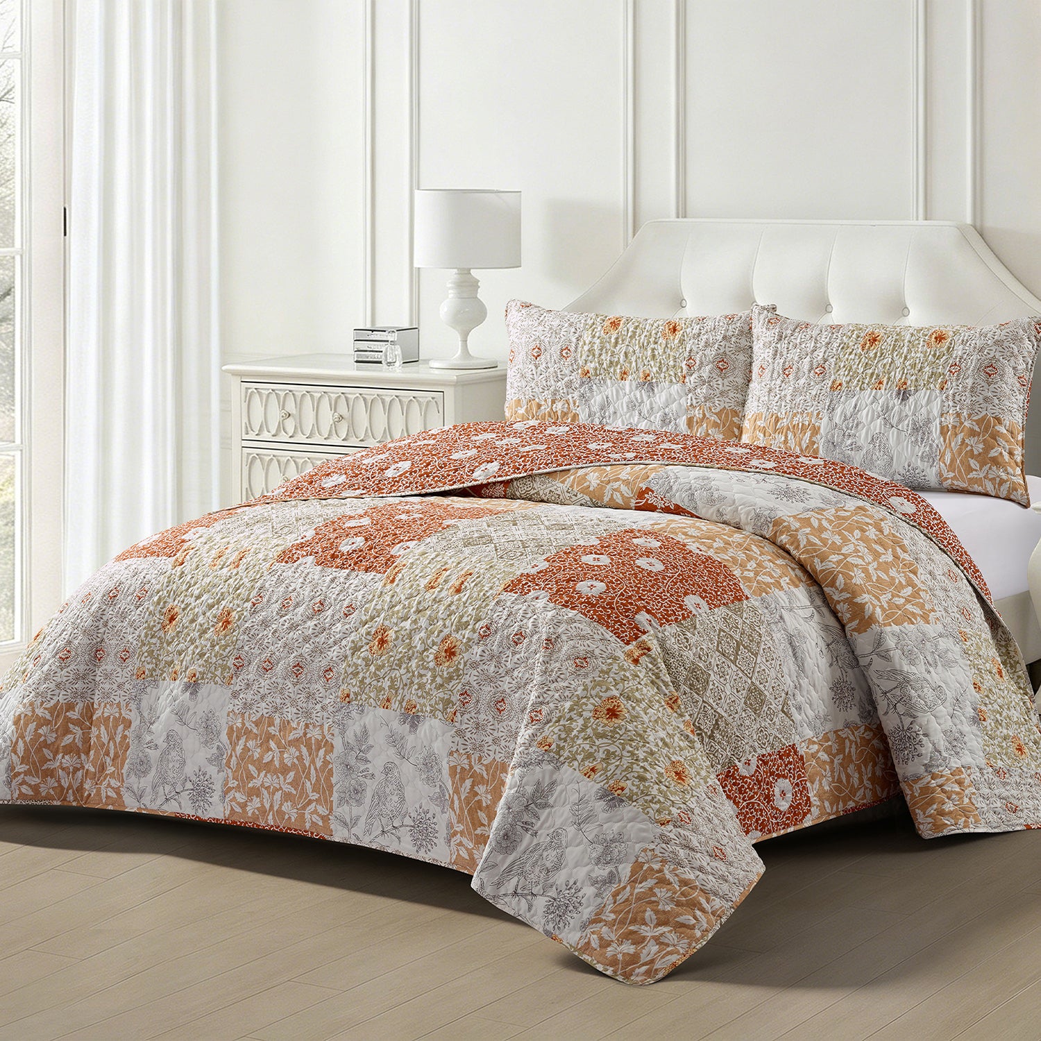 A patchwork quilt set in orange, beige, and white with matching shams, styled on a bed in a bright, modern bedroom.