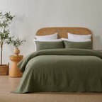 Olive green quilted coverlet styled neatly on a bed with matching pillowcases, a woven rattan headboard and natural timber décor.