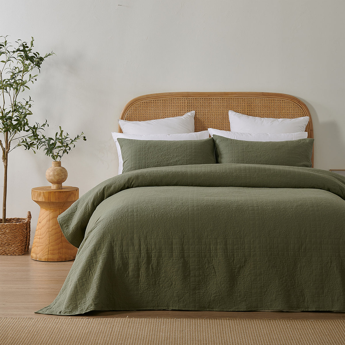 Olive green quilted coverlet styled neatly on a bed with matching pillowcases, a woven rattan headboard and natural timber décor.