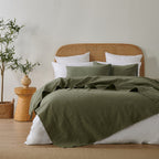 Olive green quilted coverlet styled loosely across a bed with matching pillowcases, a woven rattan headboard and natural timber décor.