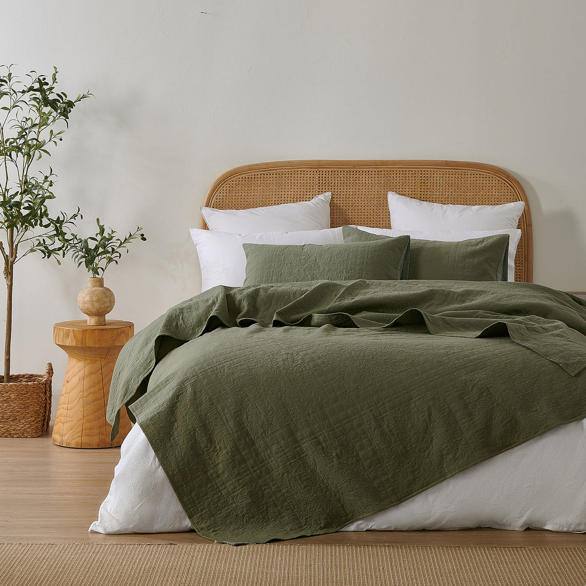 Olive green quilted coverlet styled loosely across a bed with matching pillowcases, a woven rattan headboard and natural timber décor.