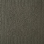 Close-up of the olive green coverlet featuring a quilted floral motif framed by a textured grid pattern.