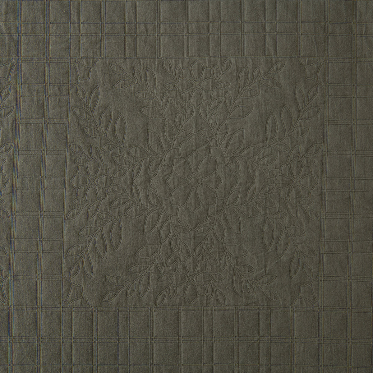 Close-up of the olive green coverlet featuring a quilted floral motif framed by a textured grid pattern.