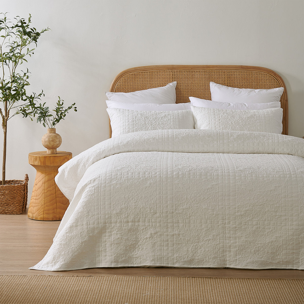 White quilted coverlet neatly styled on a bed with matching pillowcases, a woven rattan headboard and natural timber décor.