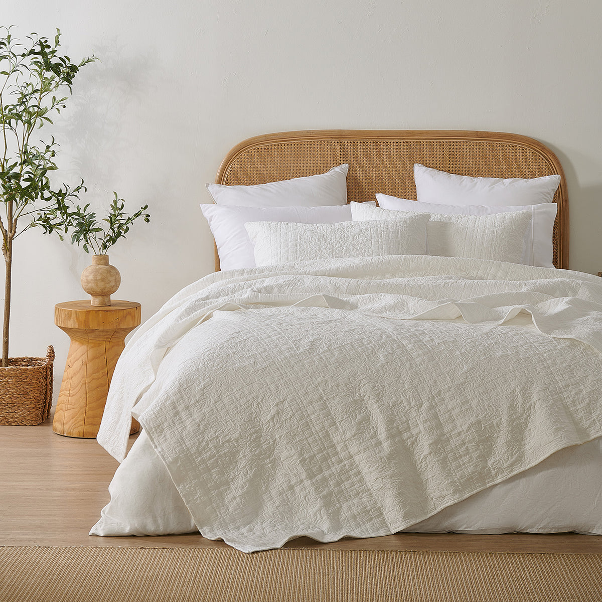 White quilted coverlet styled loosely across a bed with matching pillowcases, a woven rattan headboard and natural timber décor.