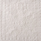 Close-up of the white quilted coverlet featuring stitched floral motifs framed by a textured grid pattern.