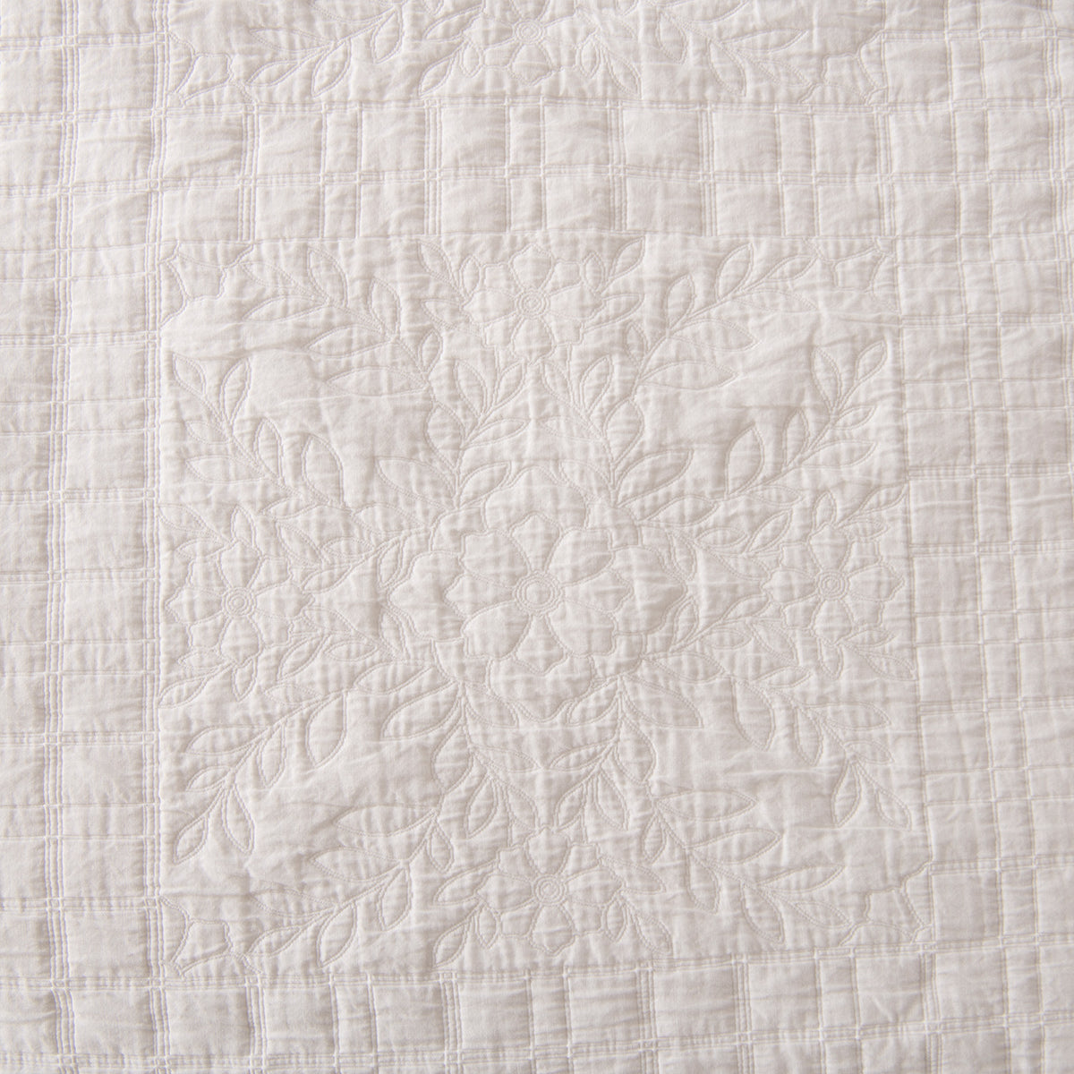 Close-up of the white quilted coverlet featuring stitched floral motifs framed by a textured grid pattern.