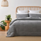 Grey quilted coverlet set styled on a bed with matching pillowcases in a bright neutral bedroom.