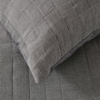 Grey quilted coverlet close-up showing textured fabric and diamond stitching detail.