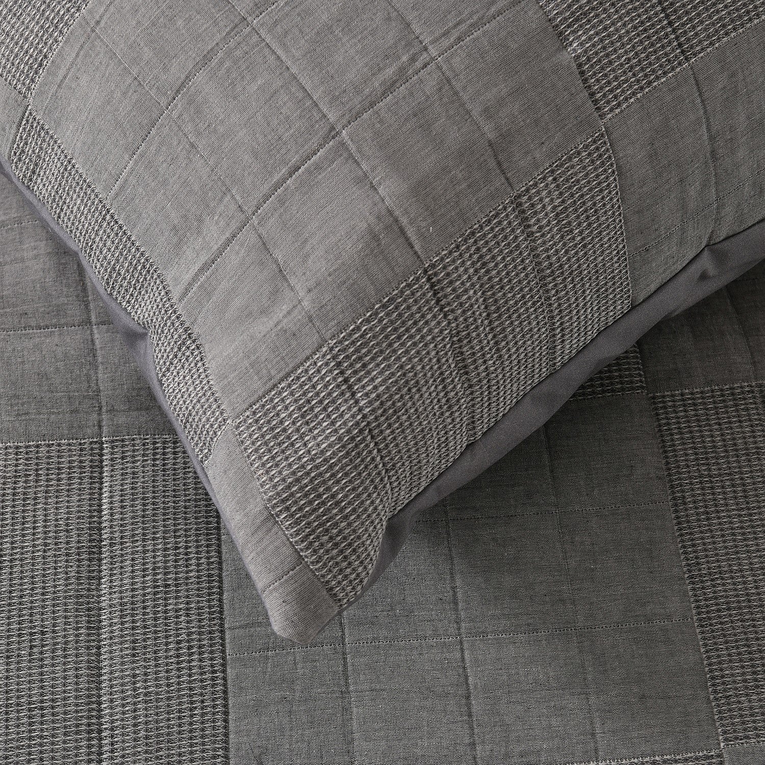 Grey quilted coverlet close-up showing textured fabric and diamond stitching detail.