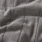 Grey quilted coverlet close-up showing textured fabric and diamond stitching detail.