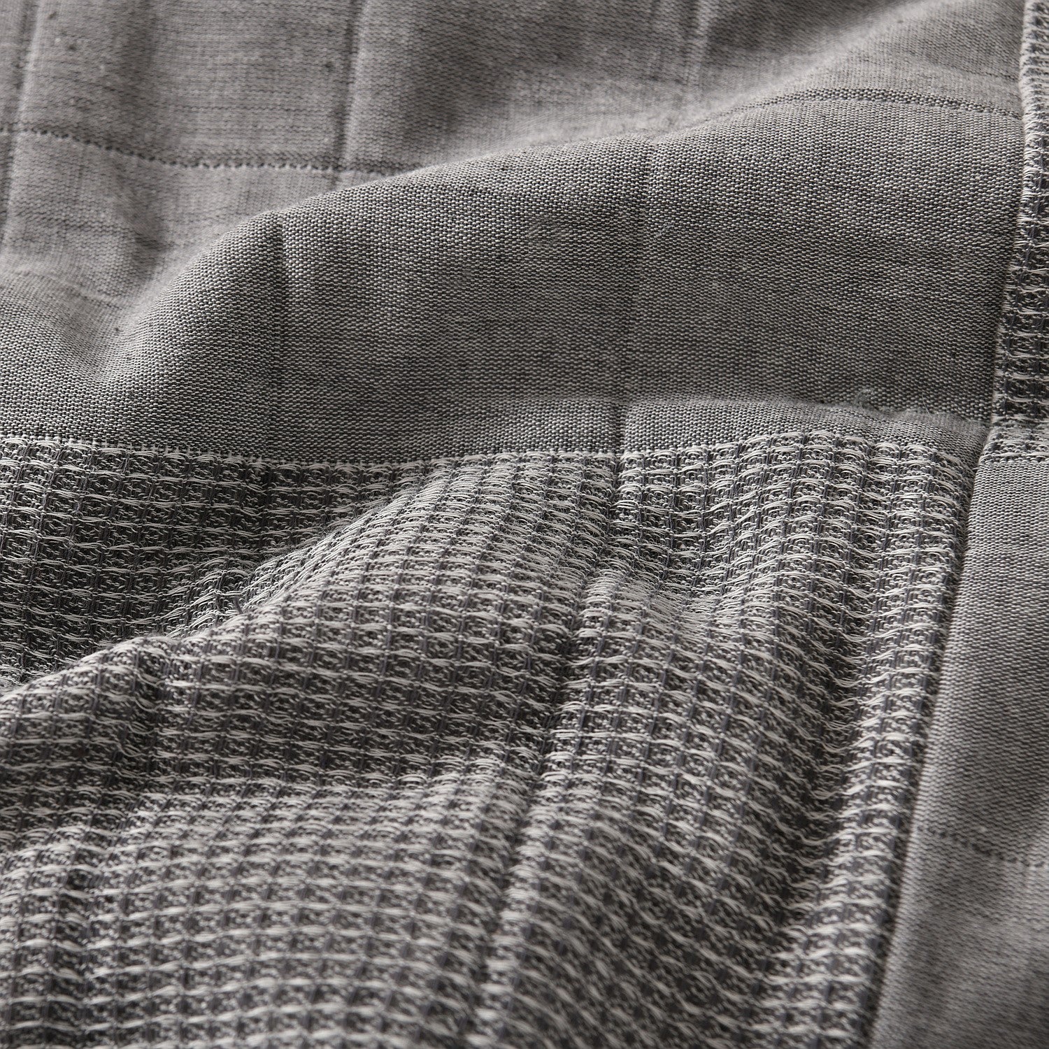 Grey quilted coverlet close-up showing textured fabric and diamond stitching detail.