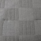 Grey quilted coverlet close-up showing textured fabric and diamond stitching detail.