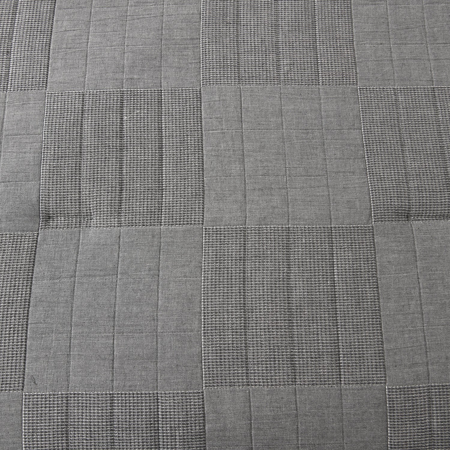 Grey quilted coverlet close-up showing textured fabric and diamond stitching detail.