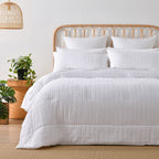 White quilted coverlet set styled on a bed with matching pillowcases in a bright neutral bedroom.
