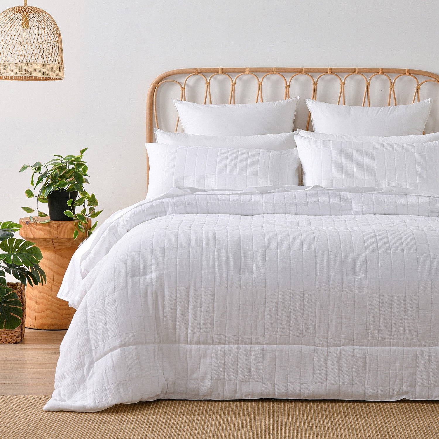 White quilted coverlet set styled on a bed with matching pillowcases in a bright neutral bedroom.