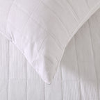 White quilted coverlet close-up showing textured fabric and diamond stitching detail.